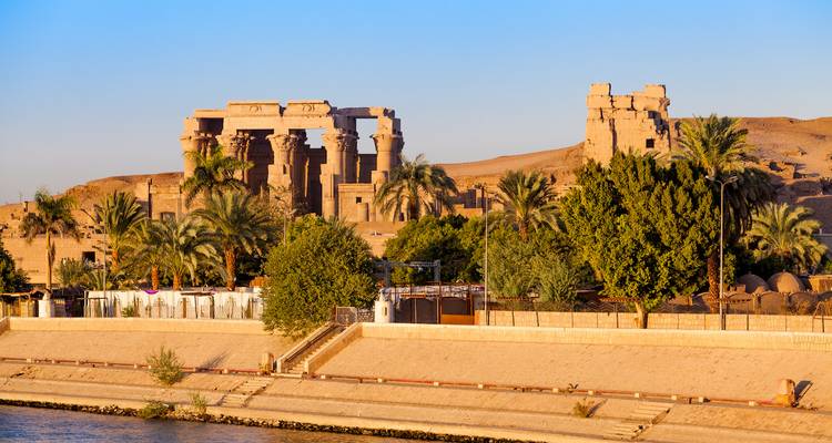 Panorama junto al río del complejo del Templo de Kom Ombo enmarcado por palmeras y la cálida luz del atardecer.