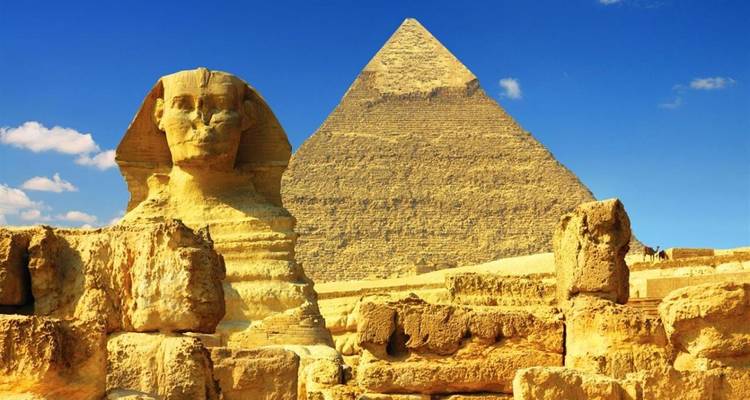 The Great Sphinx sits before the towering Great Pyramid under a vivid blue sky in the Giza desert.