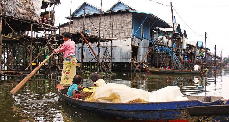 Familie navigiert mit einem Boot durch Pfahlhäuser auf dem Tonle Sap See.