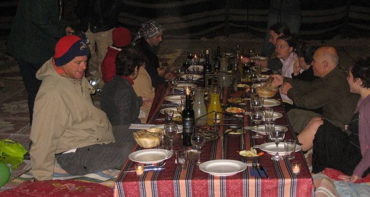 Eine Gruppe von Menschen, die um einen niedrigen Tisch sitzen und in einem Zelt eine Mahlzeit einnehmen.