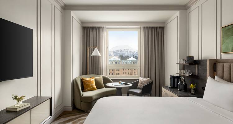 Chambre d'hôtel élégante avec mobilier moderne et vue sur les pics enneigés par la fenêtre.