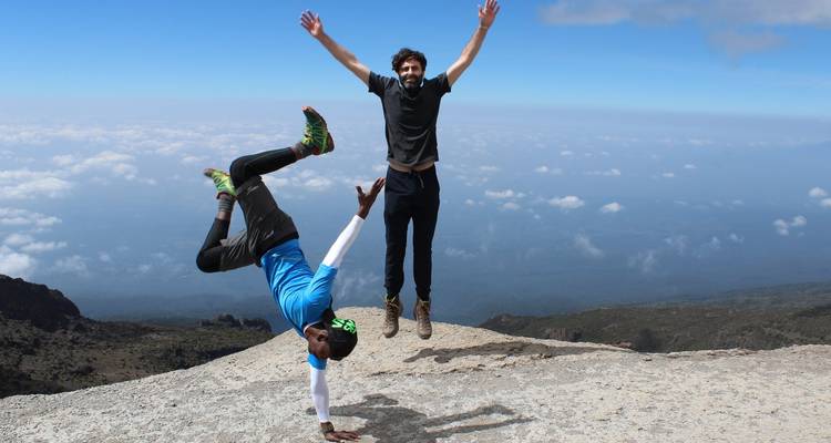 Twee mannen die acrobatiek uitvoeren op een klif met een uitgestrekt landschap.
