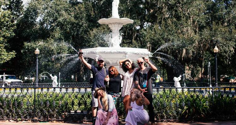 People posing in front of a fountain with lush greenery.