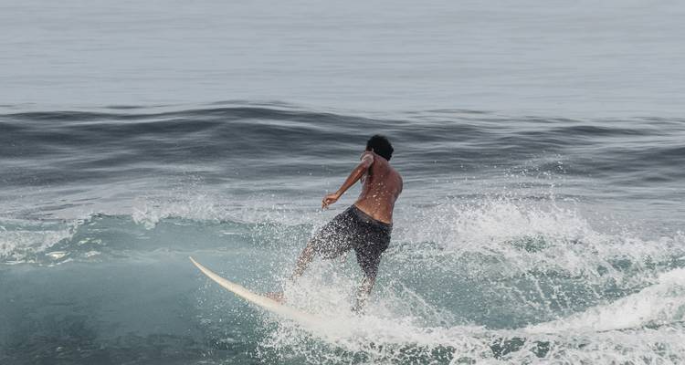 Persona surfeando en una ola en un entorno de océano vasto.