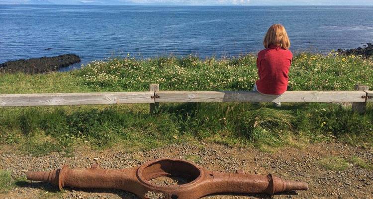 Een persoon die op een bankje zit met uitzicht op een schilderachtig zeezicht.