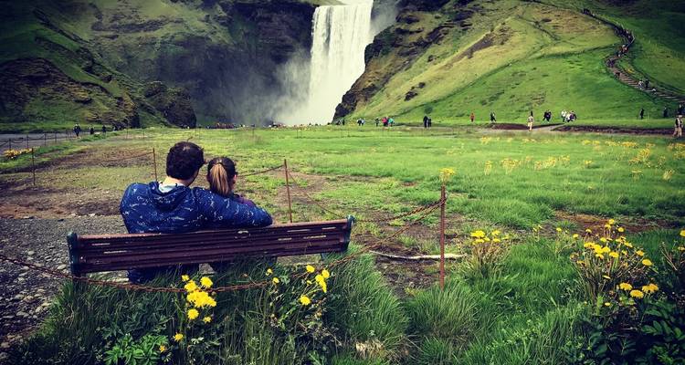 Een stel zittend op een bankje dat een waterval bewondert in een weelderige groene omgeving.