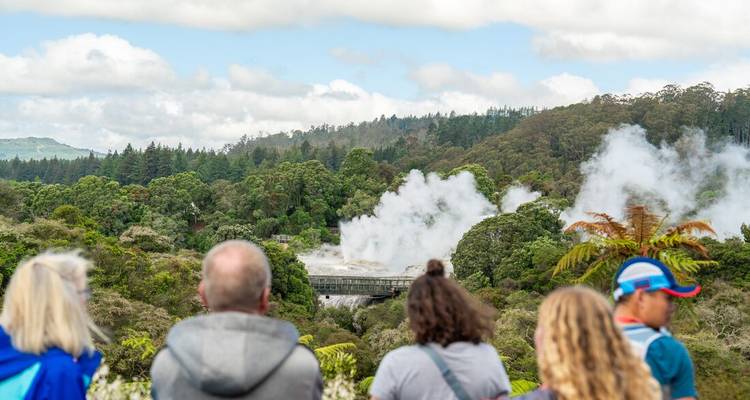 Primer plano de personas observando géiseres humeantes y exuberante vegetación.