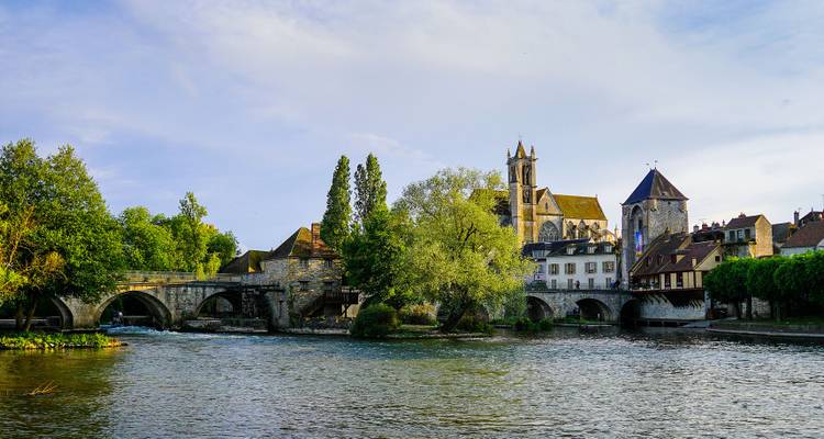 Stone bridge and medieval church reflected over a calm river in a quaint French village.