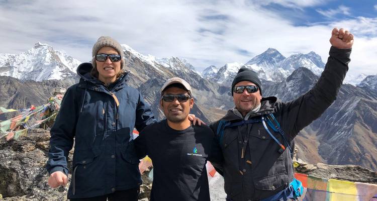 Trois personnes posant avec des montagnes enneigées en arrière-plan.