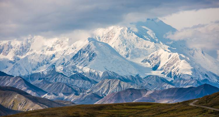 El macizo nevado de Denali se eleva sobre la tundra ondulante bajo nubes dramáticas.