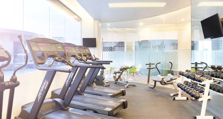 Salle de sport de l'hôtel avec équipements d'exercice et éclairage lumineux.