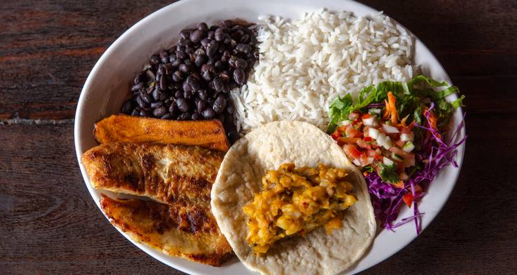 Colorful Costa Rican meal with rice, beans, plantains, tortilla and vegetables on a white plate