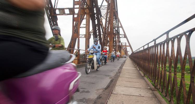 Les motos traversent à grande vitesse le Pont Long Biên rouillé en créant un flou de mouvement par un jour nuageux.