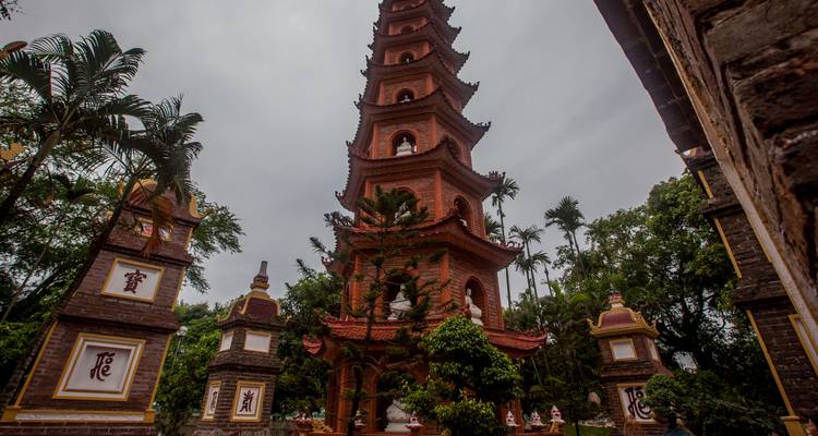 La pagode Tran Quoc aux briques rouges imposantes, entourée de verdure sous un ciel gris