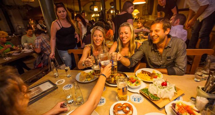 Un groupe d'amis trinque avec des chopes de bière à l'intérieur d'une animée brasserie bavaroise remplie de convives.