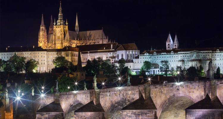 Die Prager Burg und die St.-Veits-Kathedrale strahlen über den beleuchteten Bögen der Karlsbrücke, die sich in der Moldau in der Nacht spiegeln.
