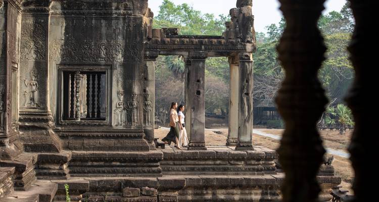 Deux voyageurs marchent parmi les colonnes de grès usées par le temps des ruines d'Angkor entourées par la jungle