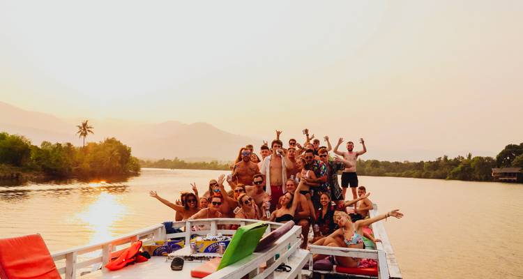 Grand groupe de voyageurs célébrant à bord d'un bateau fluvial au coucher du soleil avec des montagnes en arrière-plan