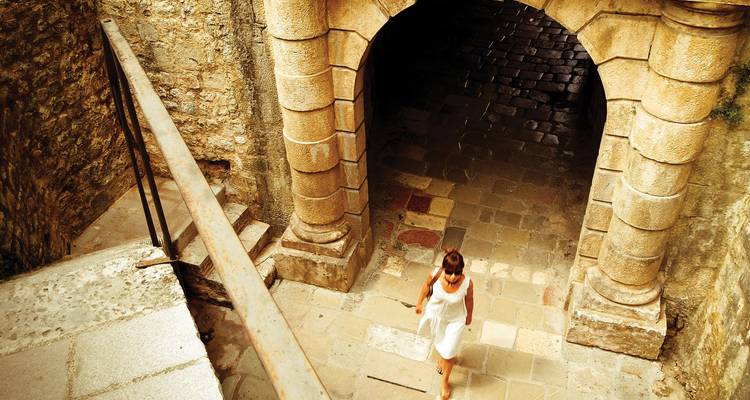 Mujer en vestido blanco bajando por escaleras de piedra histórica bajo un arco imponente