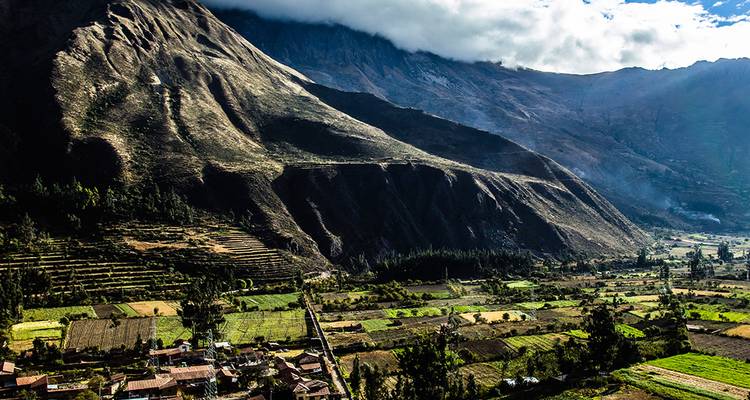 La luz matutina proyecta sombras sobre el Valle Sagrado cultivado bajo acantilados andinos imponentes.