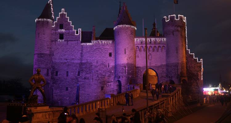 Mittelalterliche Burgmauern, die nachts mit violetten Feiertagslichtern beleuchtet sind, mit Besuchern, die durch das Tor eintreten