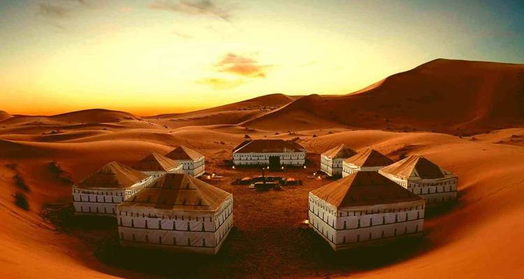 Wüstencamp mit Zelten bei Sonnenuntergang und sanften Dünen.