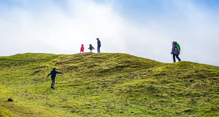 People walking on grassy hills against a bright sky.