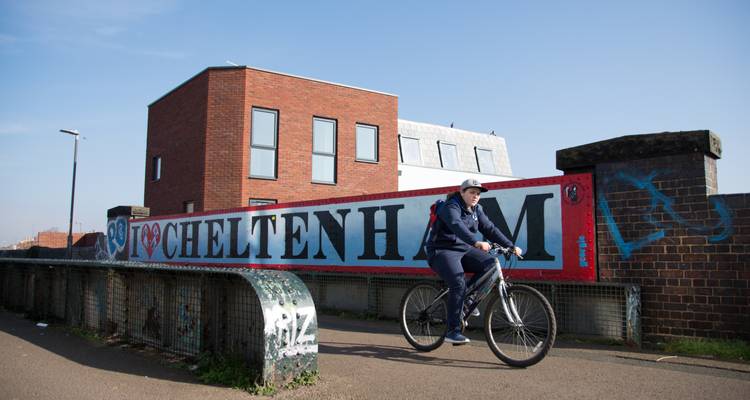 Cyclist on a bridge beside a sign for Cheltenham.