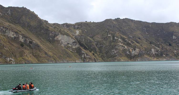 Lake surrounded by mountains with a small boat and people in life jackets.