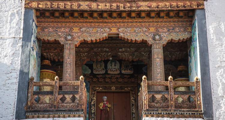 Un monje anciano se para en la entrada ricamente tallada y pintada de un monasterio adornada con patrones intrincados.