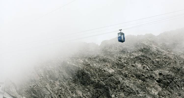 Seilbahn, die sich durch neblige Berglandschaft bewegt.