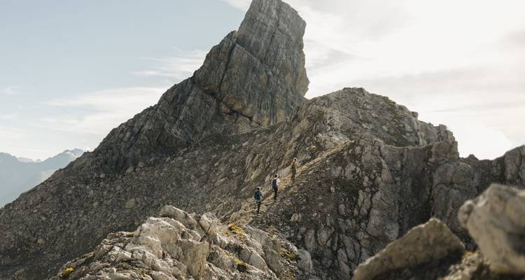 Wanderer auf einem rauen Bergpfad mit großen Felsformationen.