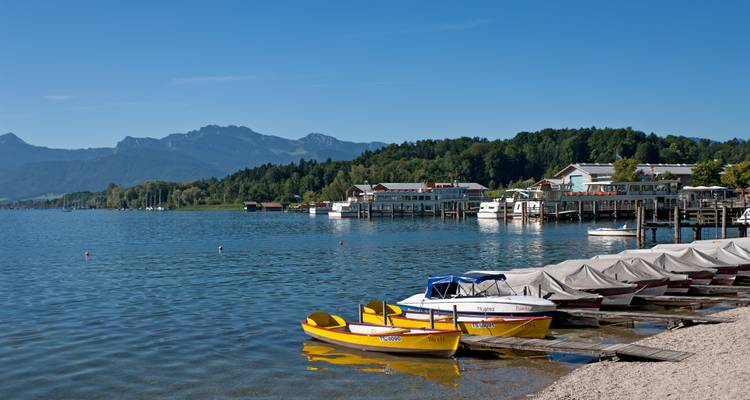 Lakeside view with anchored boats, wooden piers, and distant mountains.