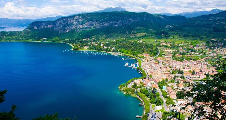 Vue aérienne d'une ville au bord d'un lac entourée de collines verdoyantes et de montagnes.