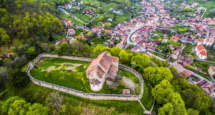 Luftaufnahme einer mittelalterlichen befestigten Kirche, umgeben von üppigem grünem Wald und einem charmanten siebenbürgischen Dorf.