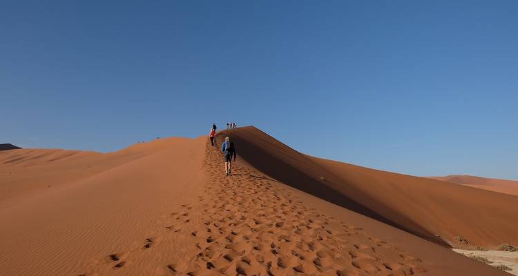 Des gens qui grimpent une dune de sable, laissant des empreintes de pas derrière eux.