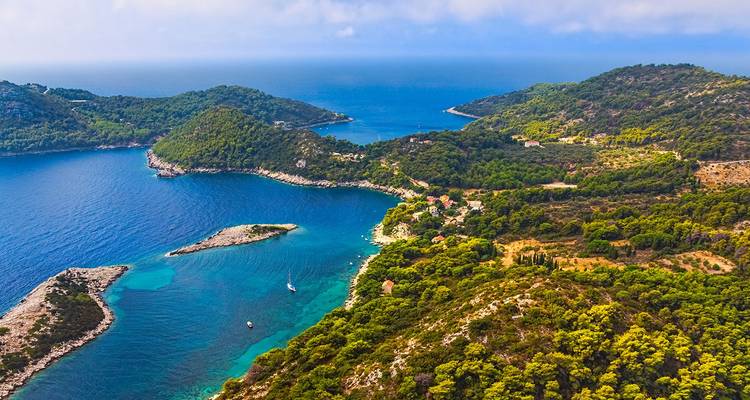 Aerial vista of rugged, forested Adriatic islands separated by sapphire channels under hazy sunshine