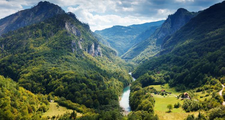 Dramatische riverkloof omzoomd door steile bosrijke bergen onder vlokkerige wolken.