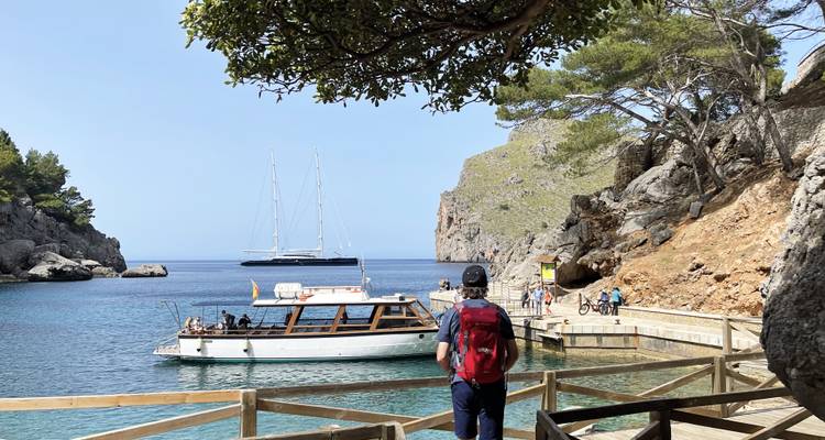 Kleiner Hafen in felsiger Bucht mit Segelbooten; Wanderer mit Rucksack betrachtet die Yachten