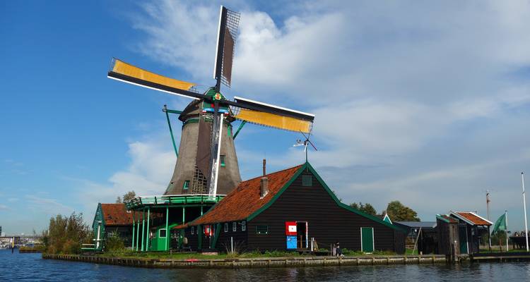 Traditional green-and-brown Dutch windmill and barns beside a quiet waterway at Zaanse Schans.