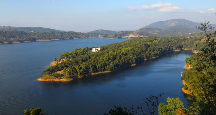 Ruhiger See umgeben von dichtem Wald und Hügeln.