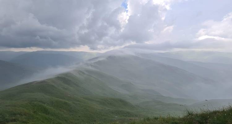 Neblige Hügel mit dramatischen Wolken darüber.