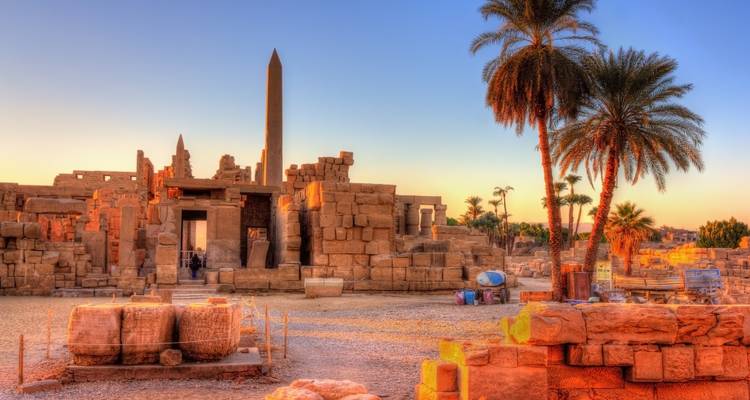 Ancient ruins with a tall obelisk at sunset.