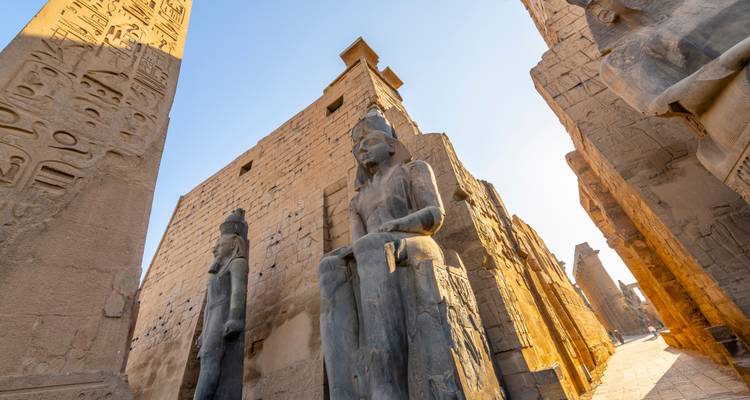 Low-angle view of colossal statues and an obelisk at Luxor Temple glowing in late afternoon light.