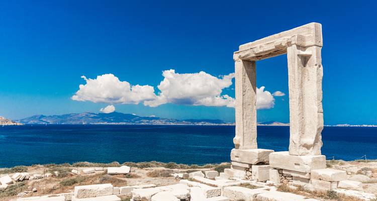 Ancient stone gateway near the sea with mountains in the distance.