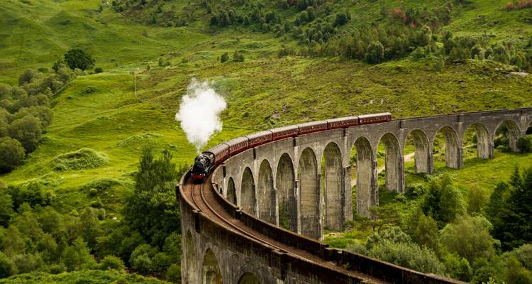 Stoomtrein die het iconische Glenfinnan Viaduct oversteekt, omringd door groene heuvels.
