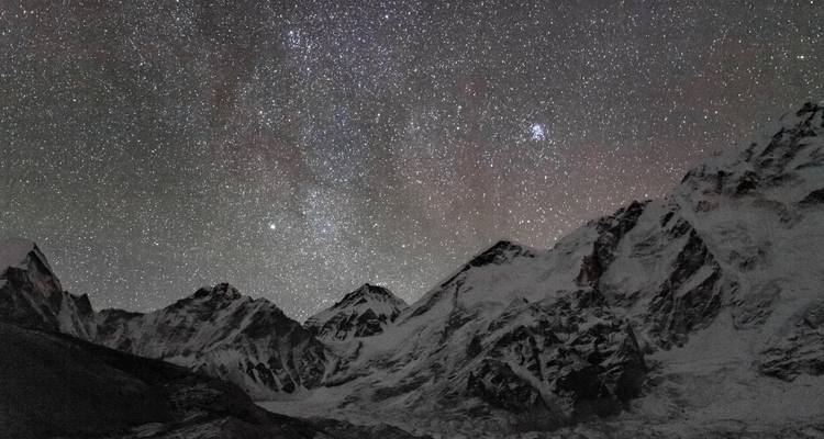 Nachthimmel voller Sterne über schneebedeckten Bergen.