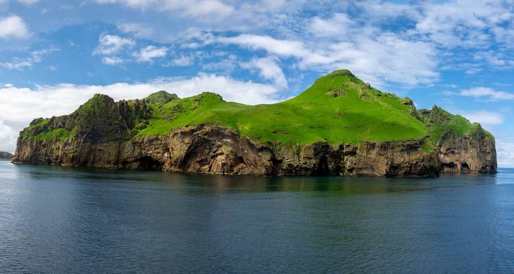 Eine üppig grüne Insel inmitten eines ruhigen Meeres unter einem blauen Himmel.