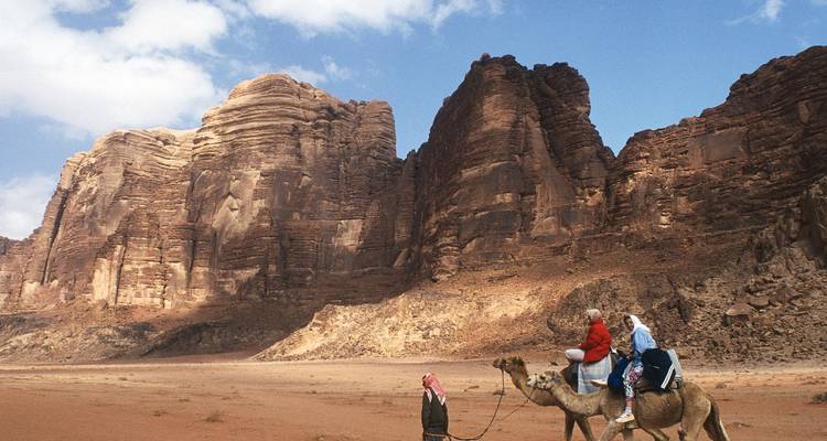 Reizigers rijden op kamelen over de spectaculaire rode woestijnkliffen van Wadi Rum.