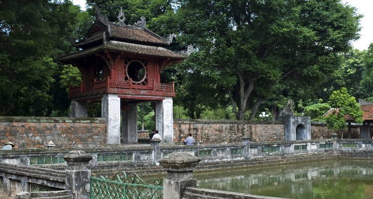 Alter Tempel mit Spiegelung in einem ruhigen Teich, umgeben von Grün.